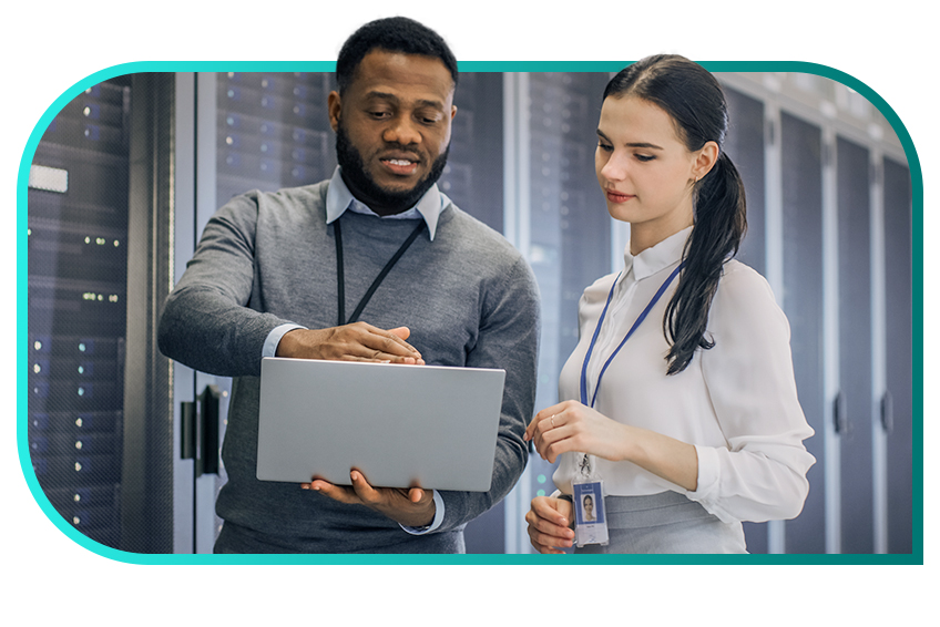 Two professionals wearing company lanyards stand in a data center and work from a laptop.