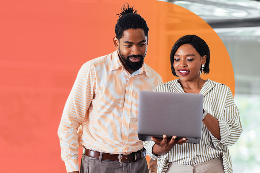 Two people stand next to each other and look at the laptop one of them is holding.