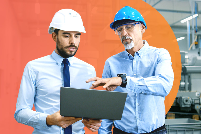 Two individuals wearing safety helmets and light blue shirts standing in an industrial setting, reviewing information on a laptop. One person is pointing at the screen while machinery and equipment are visible in the background, with an orange circular graphic overlay behind them.