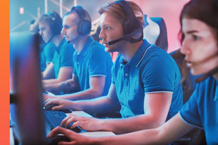 Group of gamers wearing headphones and blue polo shirts seated at computers in an esports event.