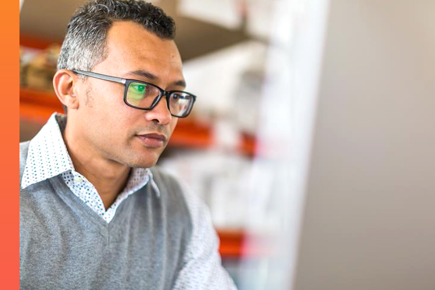 Man in wearing collared shirt and glasses works at a computer screen