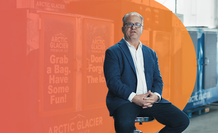 Businessman sits in front of ice freezers that have the Arctic Glacier logo on them.