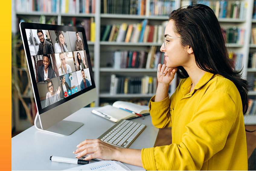 A person wearing a yellow shirt sitting in front of a computer monitor participates in a video conference call with multiple colleagues.