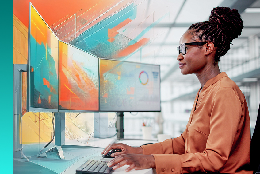 A person wearing glasses and an orange blouse works at a desk with multiple computer monitors displaying abstract graphics and data visualizations.
