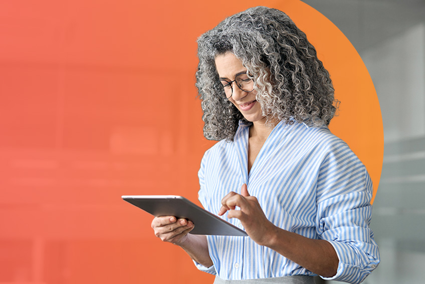 Person in a striped button-down shirt works on a tablet and smiles.