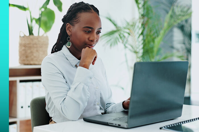 Business professional in button-down shirt sits at a desk and works on a laptop.