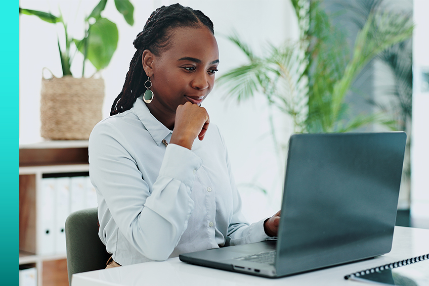 Business professional in button-down shirt sits at a desk and works on a laptop.